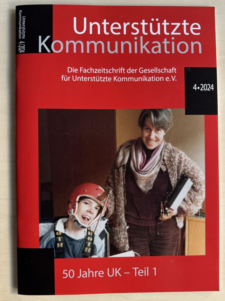 Cover der Ausgabe 4/2024 der Zeitschrift "Unterstützte Kommunikation". Zu sehen ist ein Junge, der im Rollstuhl sitzt und einen offenen Motorradhelm auf hat, auf welchem ein Kopfstab befestigt ist. Neben ihm steht eine ätere Frau mit grauen Haaren, die in die Kamera blickt.